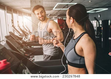 Slim Girl And Strong Guy Are Running On The Running Machine. They Are Talking With Each Other And En
