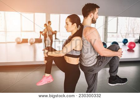 A Picture Of Man And Woman Standing Back To Back And Pulling Up One Leg. They Are Trying To Keep The