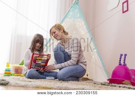 Mother And Daughter Sitting In The Playroom, Learning Summation With Abacus. Focus On The Mother