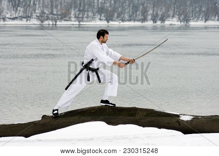 The Ninja In White Kimono With Sword Is Practicing Martial Arts On Wood On Riverside At Winter.