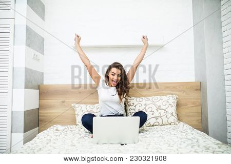 Girl With Raised Hands In Bed Using Laptop At Home