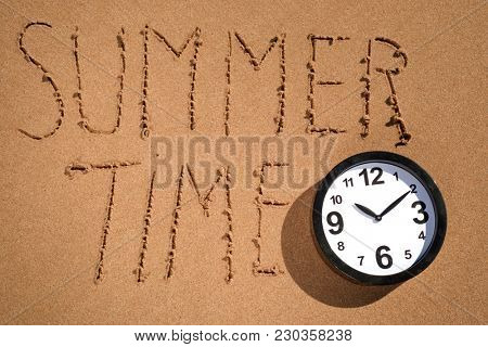 high angle view of a clock and the text summer time written on the wet sand of the seashore of a beach