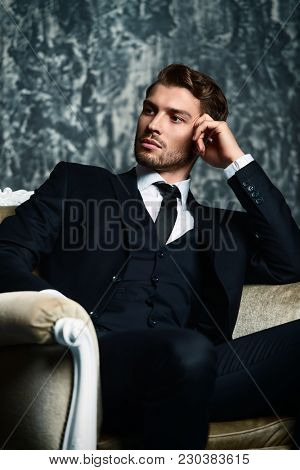 Portrait of a handsome man in an elegant suit sitting in an armchair on a grunge background. Studio shot.