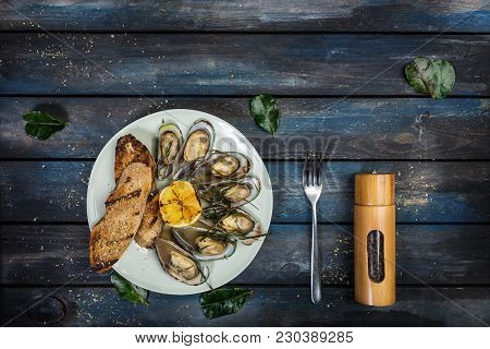 Mussels And Bread Toasts On On A White Plate. Served With Half Grilled Lemon, Fork And Leaves Of Kaf