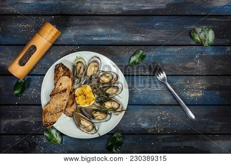 Mussels And Bread Toasts On On A White Plate. Served With Half Grilled Lemon, Fork And Leaves Of Kaf