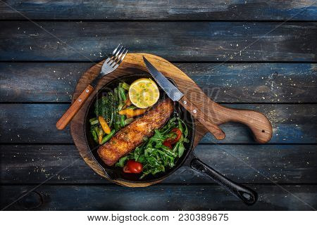 Grilled Salmon Fillet In A Frying Pan, Vegetables, Arugula With A Lemon. On The Cutting Board And Wo