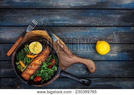 Grilled Salmon Fillet In A Frying Pan, Vegetables, Arugula With A Lemon. On The Cutting Board And Wo
