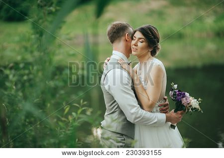 The Bride And Groom Walk On A Background Of Lake. Romantic Wedding Photo.
