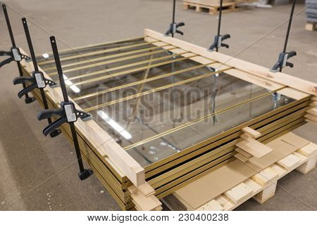 production, manufacture and industry concept - mirror panels loaded on palette and fastened by bar clamps at furniture factory workshop