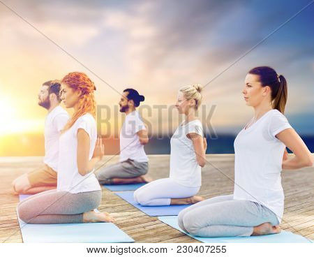 fitness and healthy lifestyle concept - group of people doing yoga reverse prayer pose on wooden pier over sea background