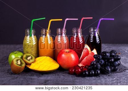 Fresh Color Juices Smoothie with a straw Violet Green Yellow Orange Red from Tropical Fruits Kiwi Melon Strawberry Apple Orange Banana Pine Apple Mango Pomegranate Grape Bottles Rainbow Dark Background.