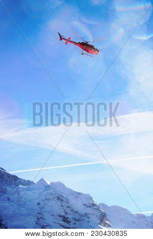 Red Helicopter Flying Over Swiss Alpine Mountain Mannlichen In Winter, Switzerland