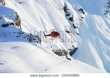 Red Helicopter Flying Near Swiss Alpine Mountain Mannlichen In Winter, Switzerland