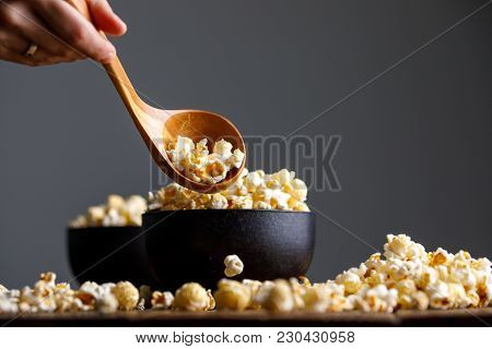A Ceramic Bowl Full Of Popcorn And A Hand With A Wooden Spoon Scoops It.