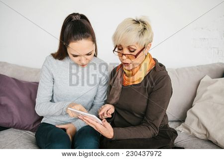 A Young Girl Volunteer Or Granddaughter Explains To An Elderly Woman How To Use A Tablet Or Shows So
