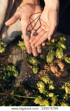 Svarog Amulets Are Held In Hands. In The Background Hops, Wheat Seeds, Walnuts, Alatyr.