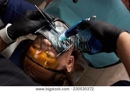 Dentist Performs Dental Treatment To A Patient In Orange Dental Glasses With A Rubberdam
