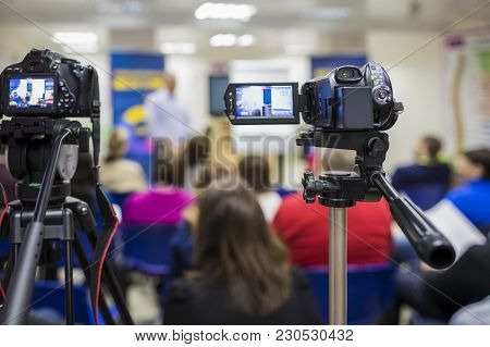 Two Video Camcoders Shot During A Conference. Pointed To A Male Host Standing In Front Of The Group 