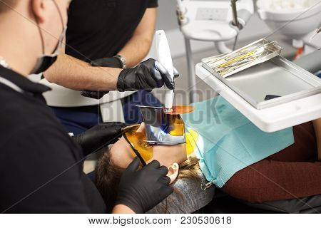 Two Dentists In Black Suits Fixing The Teeth Of A Patient With A Kofferdam On The Face
