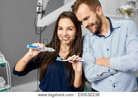 Two Young People Being Happy, A Beautiful Brunette Woman Is Squeezing A Toothpaste And A Smart Male