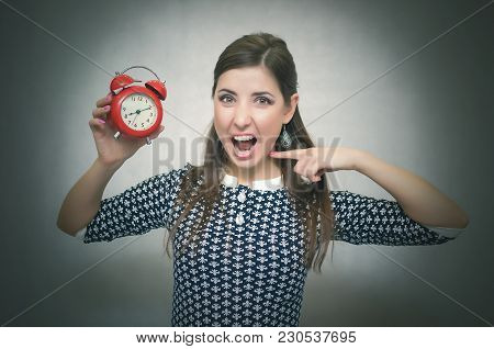 Angry Woman Holding In Hands A Red Alarm Clock And Showing On It By Her Finger And Shouting. Wicked 