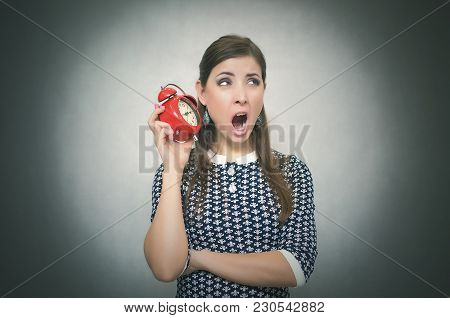 Sleepy Woman Holding In Hands Alarm Clock And Looking Aside. Latecomer Student Or Emloyee. Be Late A