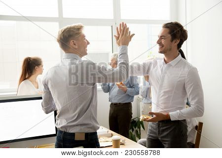 Smiling Male Coworkers Giving High Five Eating Pizza Together At Office Break, Happy Young Men Colle
