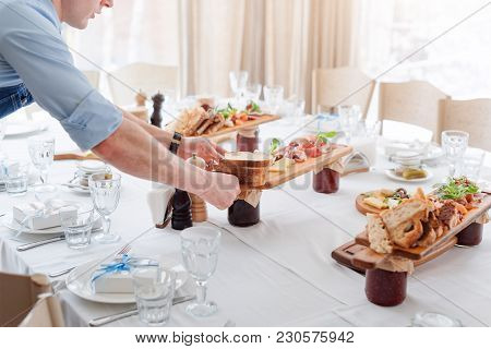 Waiter Serving Meat Dishes On Wooden Board At Restaurant, Close Up View