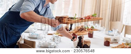 Waiter Serving Meat Dishes On Wooden Board At Restaurant, Close Up View