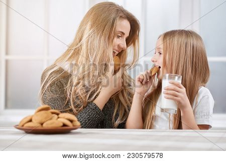 Portarait Of Older And Younger Sisters Eating Cookies And Smile.