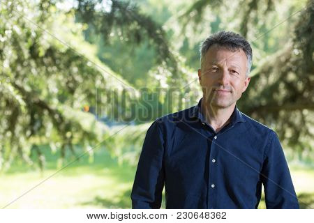 Handsome middle-aged man in park near pine tree. Attractive mid adult male model posing outddor. 