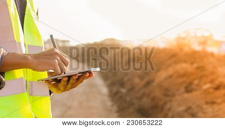 Asian Engineer With Hardhat Using  Tablet Pc Computer Inspecting And Working At Construction Site