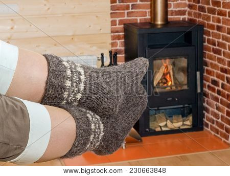 Pair Of The Thick Gray Wool Hand-knitted Socks On Women Legs Against The Background Of A Burning Fir