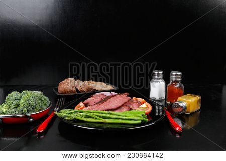 business lunch fresh roast beef meat slices on black plate wotj cutlery asparagus boiled broccoli rye bun on wooden table