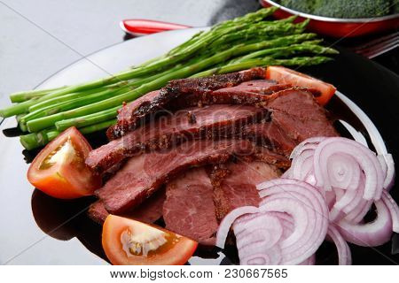 business lunch fresh roast beef meat slices on black plate wotj cutlery asparagus boiled broccoli rye bun on wooden table