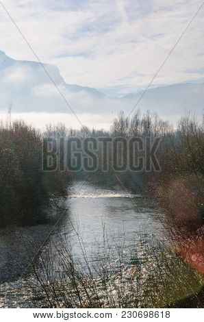 Tree-filled River Banks Near The Town Of Echelles, In The French Savoy Eary, On A Dramatically Cloud