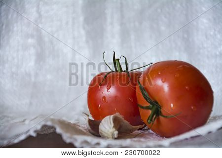 Two Red Tomatoes With Garlic On Table On Blurred Light Background. Close Up Photo