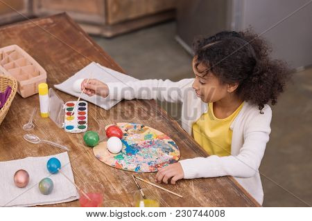 High Angle View Of African American Kid Putting Brush Into Watercolor Paints For Painting Easter Egg