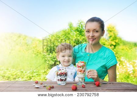 Happy Loving Family. Mother And Her Son Child Boy Are Eating Laered Dessert In Sunny Day In Green Ga