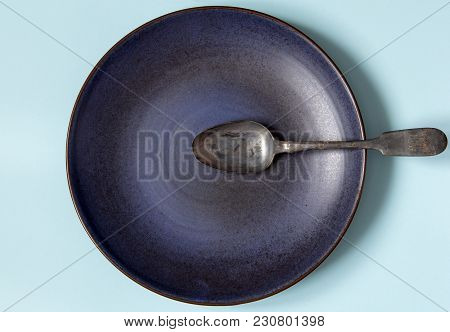 Empty Ceramic Round Plate And Spoon On Background In Blue Pastel Colors.  Top View With Copy Space.