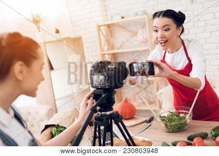 Two Culinary Bloggers In Red Aprons Taking Selfie With One Girl Behind Camera.