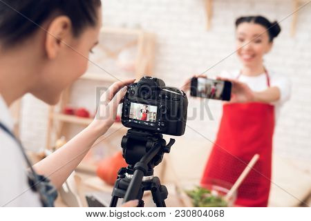 Two Culinary Bloggers In Red Aprons Taking Selfie With One Girl Behind Camera.