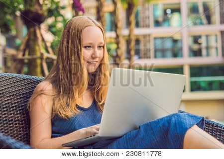 Young Female Freelancer Sitting Near The Pool With Her Laptop In The Hotel Browsing In Her Smartphon