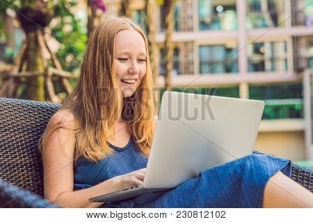 Young Female Freelancer Sitting Near The Pool With Her Laptop In The Hotel Browsing In Her Smartphon