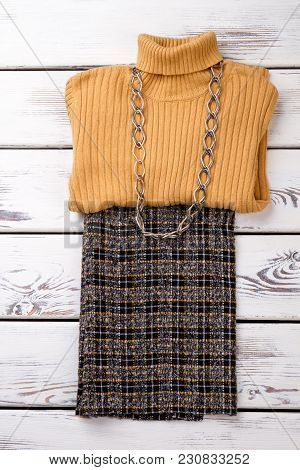 Stylish Female Clothes Set With Necklace. Folded Yellow Woolean Sweater, Checkered Trousers And Chai