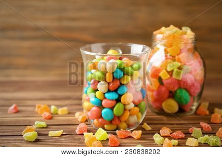 Glassware with colorful candies and succades on wooden background