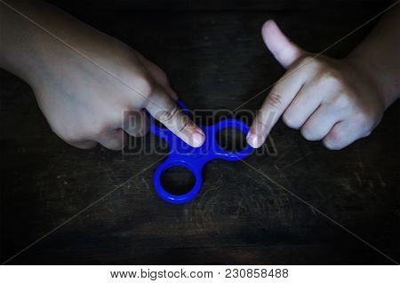 Hand Holding Fidget Spinner. Stress Relieving Toy. Child Plays With The Spinner In Blue On A Wooden 
