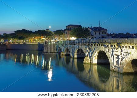 RIMINI, ITALY - JUNE 13, 2017: Night view to the bridge of Tiberius, Ponte di Tiberio across Marecchia river. The bridge was erected in 20 AD during Tiberius reign, but works started during Augustus