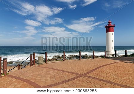 Walkway With Metal Barrier Against Red And White Lighthouse