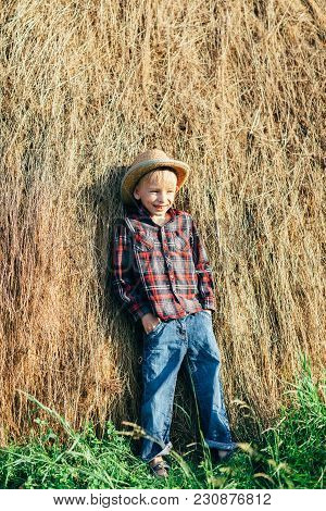 Full Length Portrait Of Boy In Pose Of Lazy Farmer, Leaning Haystack. Young Prankster Posing Against